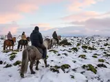 Riders on shaggy Icelandic horses crossing a snowy, moss-covered lava field
