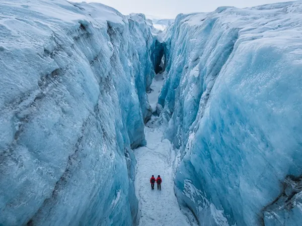 Two hikers in red jackets at the bottom of a deep blue ice canyon on a glacier