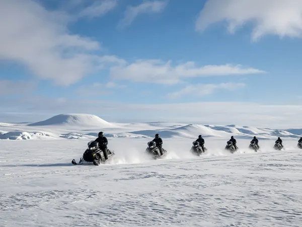 A line of snowmobiles crossing a white glacier ice cap under a blue sky